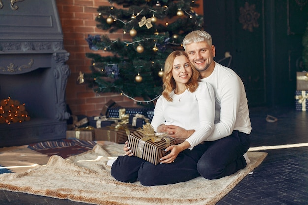 Elegante pareja sentada en casa cerca del árbol de navidad