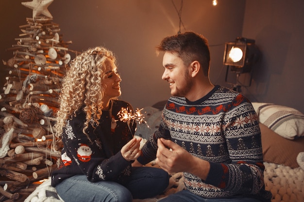 Elegante pareja sentada en casa cerca del árbol de navidad