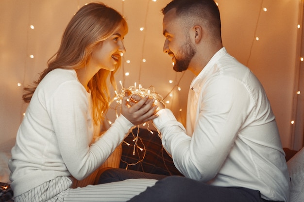 Elegante pareja sentada con una guirnalda en casa en una cama