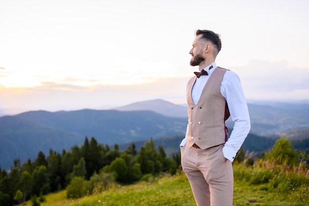 Elegante prometido posando en la cima disfrutando de la vista de las montañas