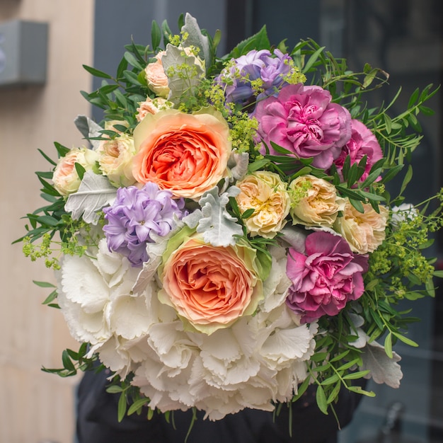 Un elegante ramo de flores blancas, naranjas, amarillas y moradas con hojas decorativas de color verde.