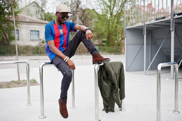 Elegante ropa de niño afroamericano en camiseta de fútbol y gafas de sol posadas en barandillas de acero Retrato de hombre deportivo negro