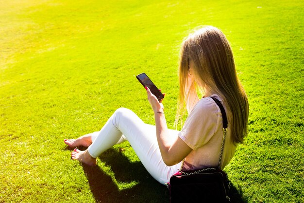 Elegante señora verifica su Smartphone sentado en el césped verde en el parque