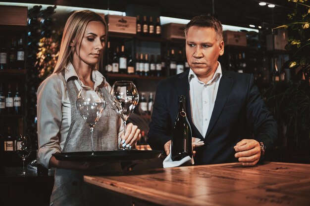 El elegante sommelier de vinos y su atractivo asistente están listos para probar nuevos vinos en una boutique de vinos privada.