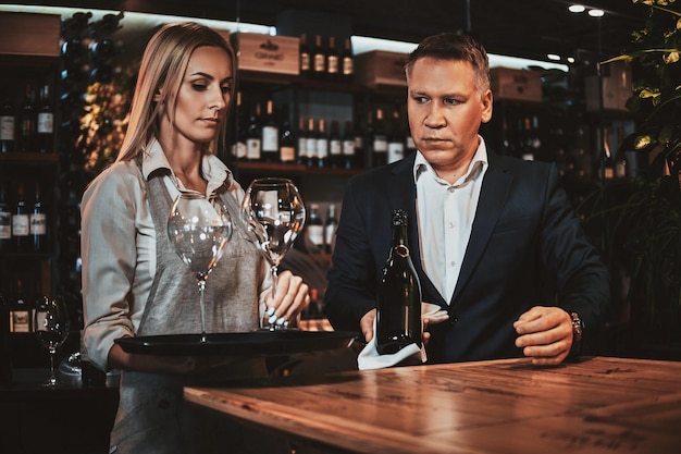 El elegante sommelier de vinos y su atractivo asistente están listos para probar nuevos vinos en una boutique de vinos privada.