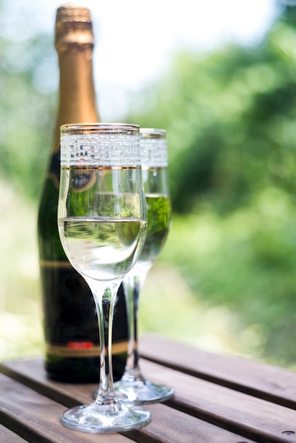 Elegantes copas de champán con botella de champán en mesa de madera