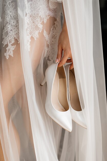 Elegantes zapatos de boda blancos en la mano de la novia