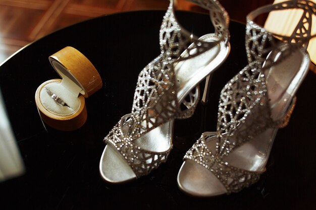Elegantes zapatos plateados y rico anillo de bodas se encuentran en la mesa negra