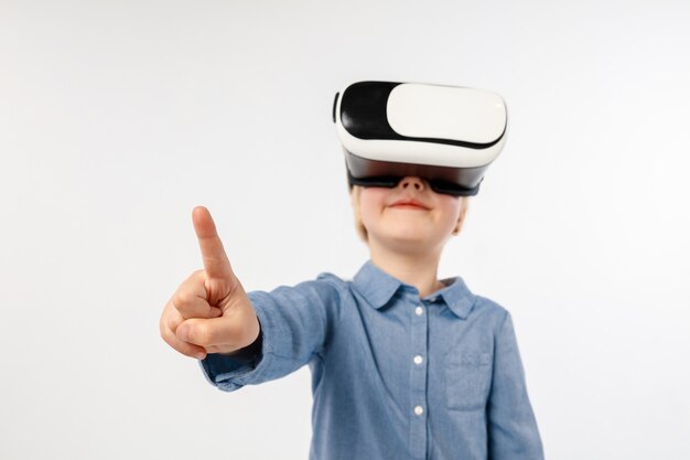 Elige la diferencia. Niña o niño apuntando al espacio vacío con gafas de realidad virtual aisladas sobre fondo blanco de estudio. Concepto de tecnología de punta, videojuegos, innovación.