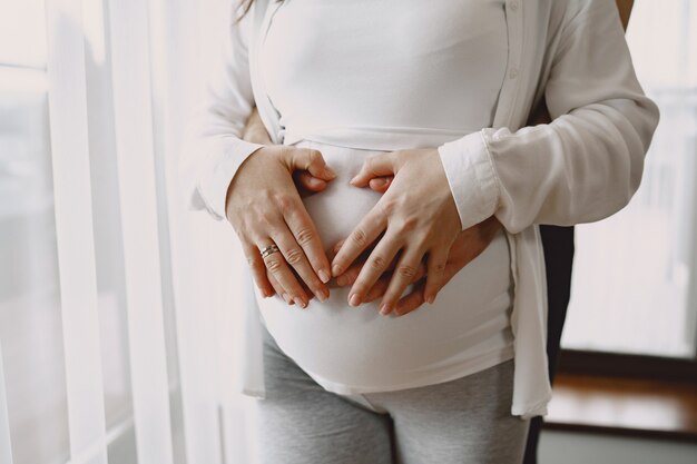 Embarazada con ropa ligera. Manos sobre el vientre de una mujer embarazada. Familia por ventana.