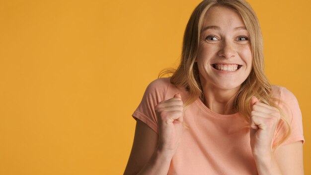 Emocionada y alegre chica rubia regocijándose en la cámara con espacio para copiar texto o contenido promocional cerca del fondo amarillo