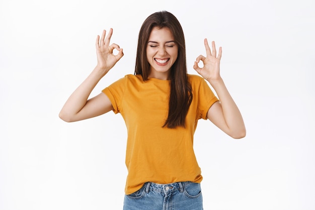 Emocionada, alegre, feliz, mujer joven con camiseta amarilla, creo que la fiesta es increíble, divertirse, disfrutar de un ambiente agradable, cerrar los ojos y sonreír complacido, mostrar bien, bien, gesto, fondo blanco.