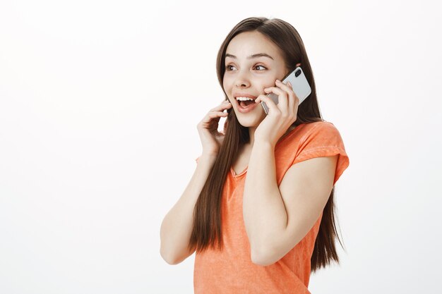 Emocionada chica atractiva sonriente hablando por teléfono móvil y mirando divertido