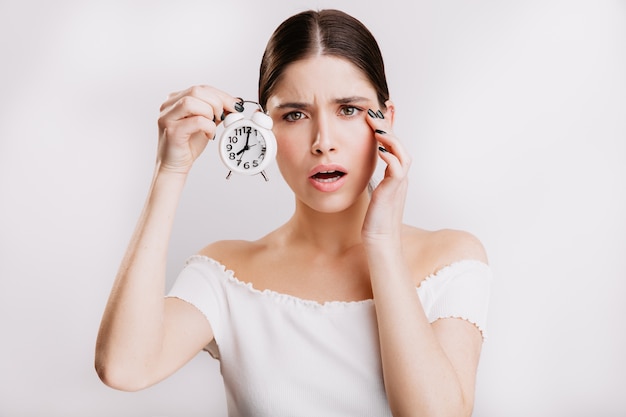 Emocionada chica de ojos verdes en la pared blanca. Mujer alarmada por la fugacidad del tiempo.