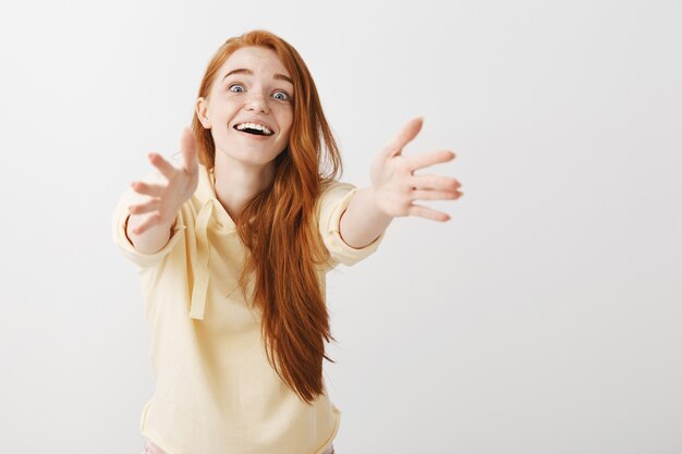 Emocionada chica pelirroja tentadora sonriendo y extendiendo las manos hacia adelante para sostener algo