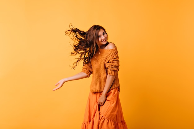 Emocionada chica de pelo largo con linda sonrisa bailando en amarillo. Señora blanca bien vestida que expresa emociones positivas.