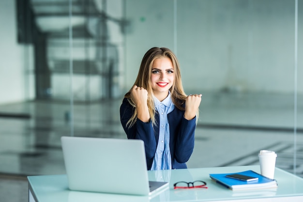 Emocionada empresaria ganando tras logro leyendo un teléfono inteligente sentado en un escritorio en la oficina