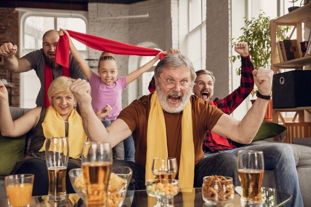 Emocionada, feliz gran familia viendo fútbol, fútbol, baloncesto, hockey, tenis, partido de rugby en el sofá de casa. Fans emocionados animando a su equipo nacional favorito. Deporte, TV, campeonato.