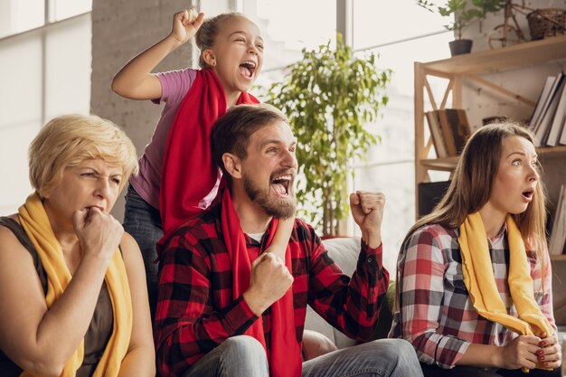 Emocionada, feliz gran familia viendo fútbol, fútbol, baloncesto, hockey, tenis, partido de rugby en el sofá de casa. Fans emocionados animando a su equipo nacional favorito. Deporte, TV, campeonato.