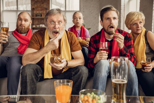 Emocionada, feliz gran familia viendo fútbol, fútbol, baloncesto, hockey, tenis, partido de rugby en el sofá de casa.