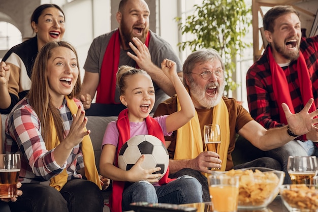 Emocionada, feliz gran familia viendo fútbol, partido de fútbol en el sofá de casa. Fans emocionados animando a su equipo nacional favorito. Divirtiéndose de abuelos a niños. Deporte, TV, campeonato.