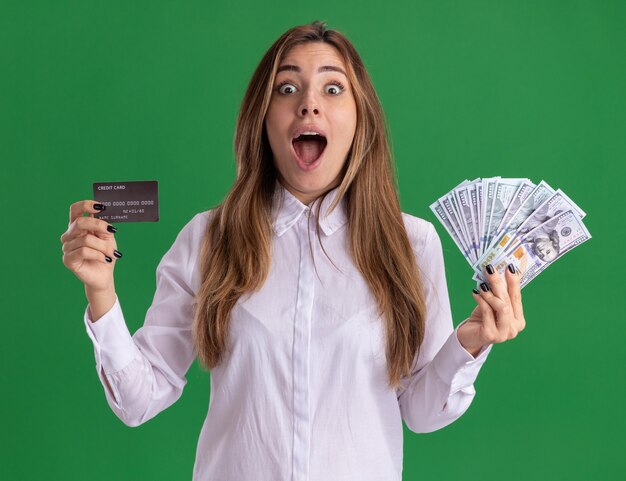 Emocionada joven bastante caucásica tiene dinero y tarjeta de crédito en verde