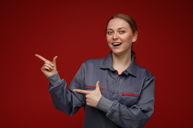 Emocionada joven ingeniera rubia vistiendo uniforme apuntando al lado