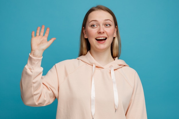 Emocionada joven mujer rubia mirando al lado haciendo gesto de hola