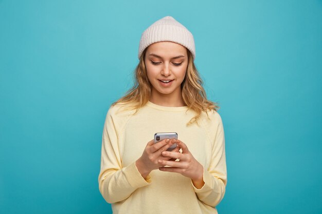 Emocionada joven vistiendo gorro de invierno con su teléfono móvil