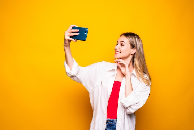 Emocionada joven vistiendo ropa casual que se encuentran aisladas sobre la pared amarilla, tomando selfie con la mano extendida