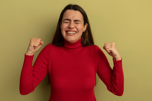 Emocionada mujer bonita caucásica se encuentra con los ojos cerrados y mantiene los puños en verde oliva