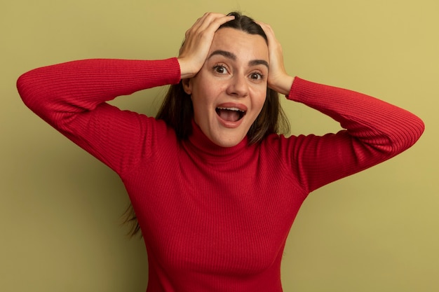 Foto gratuita emocionada mujer bonita caucásica sostiene la cabeza con las dos manos en verde oliva