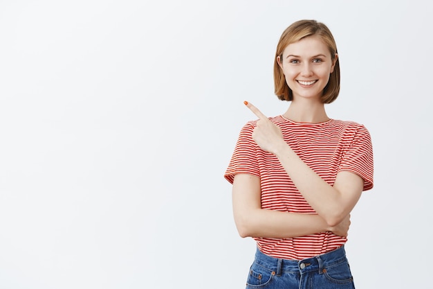 Emocionada mujer bonita feliz sonriendo, apuntando hacia la esquina superior izquierda