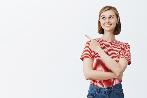 Emocionada mujer bonita feliz sonriendo, apuntando hacia la esquina superior izquierda