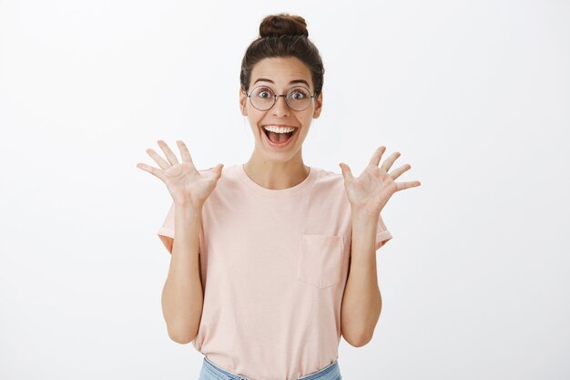 Emocionada mujer elegante joven sonriente posando contra la pared blanca