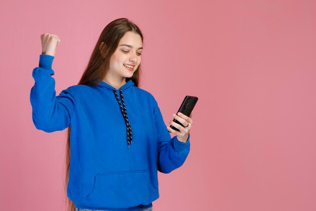 Foto gratuita emocionada mujer encantada con un teléfono inteligente levantando el puño mostrando un gesto ganador en el interior