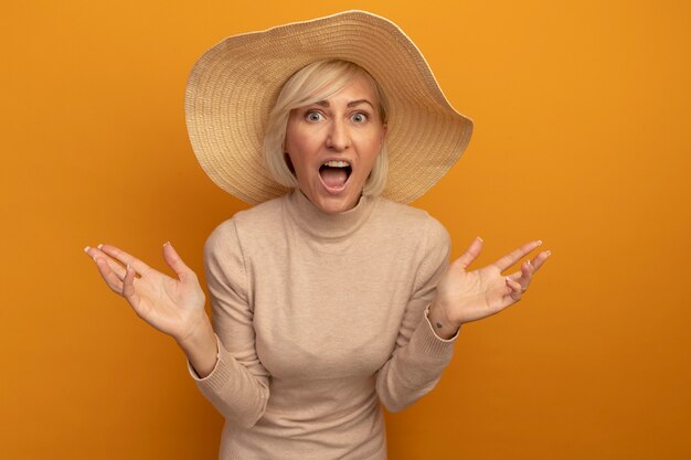 Emocionada mujer eslava rubia bonita con sombrero de playa tiene las manos abiertas y parece aislado