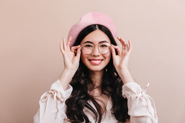 Emocionada mujer japonesa posando con gafas. Hermosa mujer asiática en boina riéndose de la cámara.