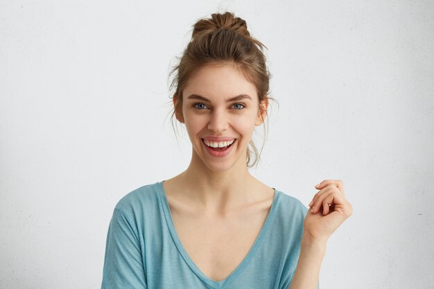 Emocionada mujer joven sonriente con nudo de pelo expresando emociones positivas mientras posa