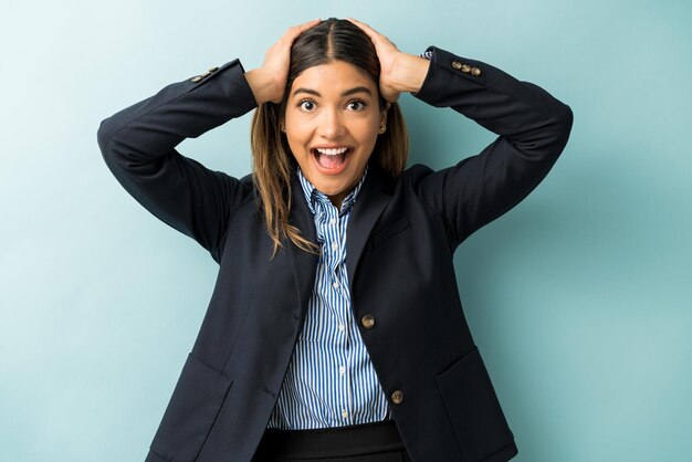 Emocionada mujer de negocios con la cabeza entre las manos de pie sorprendida contra el fondo azul.