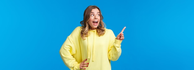 Foto gratuita emocionada y sin palabras, la chica rubia feliz reacciona a las increíbles noticias señalando y mirando la copia en blanco izquierda sp