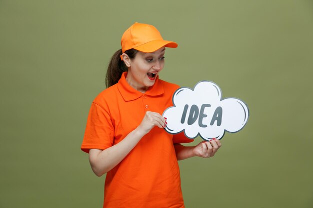 Emocionada repartidora de mediana edad con uniforme y gorra sosteniendo una burbuja de ideas mirándola aislada en un fondo verde oliva