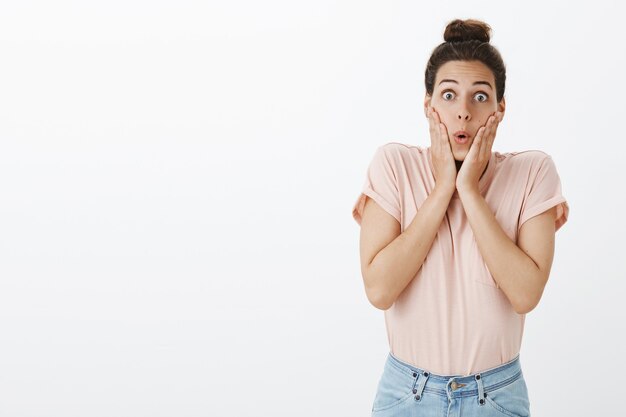 Emocionada y sorprendida joven elegante posando contra la pared blanca