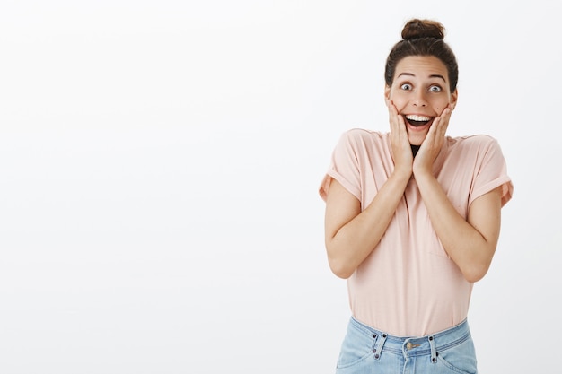 Emocionada y sorprendida joven elegante posando contra la pared blanca