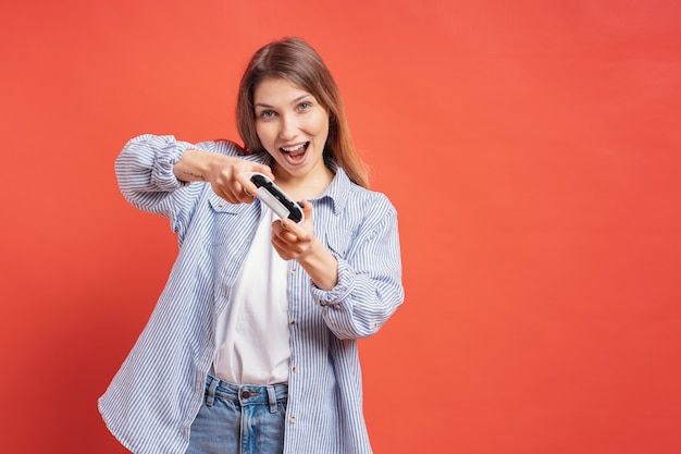 Emocionado casual joven jugando videojuegos divirtiéndose en la pared roja