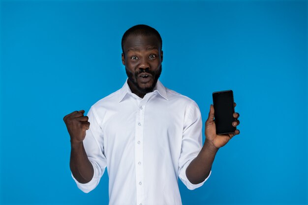 Emocionado chico afroamericano barbudo está mostrando teléfono celular
