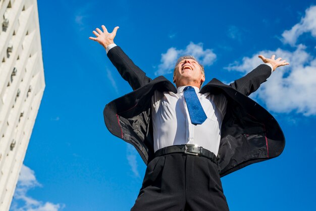 Emocionado empresario levantando sus brazos contra el cielo