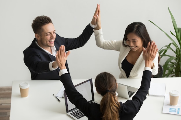 Emocionado equipo multirracial tomados de la mano dando alta celebrando el éxito cinco