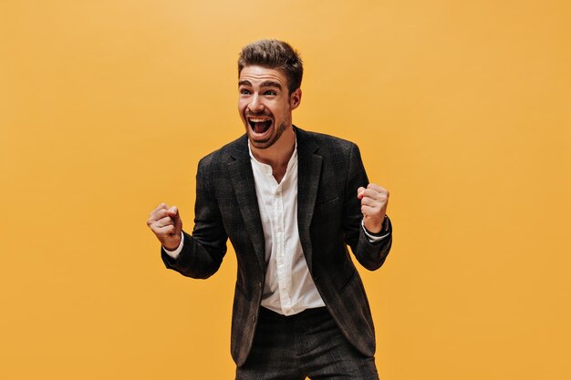 Emocionado, feliz, barbudo y se regocija con el fondo naranja. Un joven emocional con traje a cuadros y camisa blanca se ríe de forma aislada.