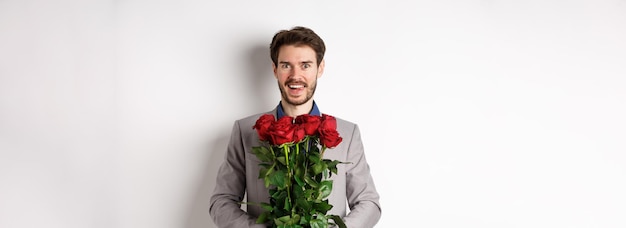 Emocionado hombre guapo en traje con ramo de rosas para una cita romántica con el amante de pie feliz en